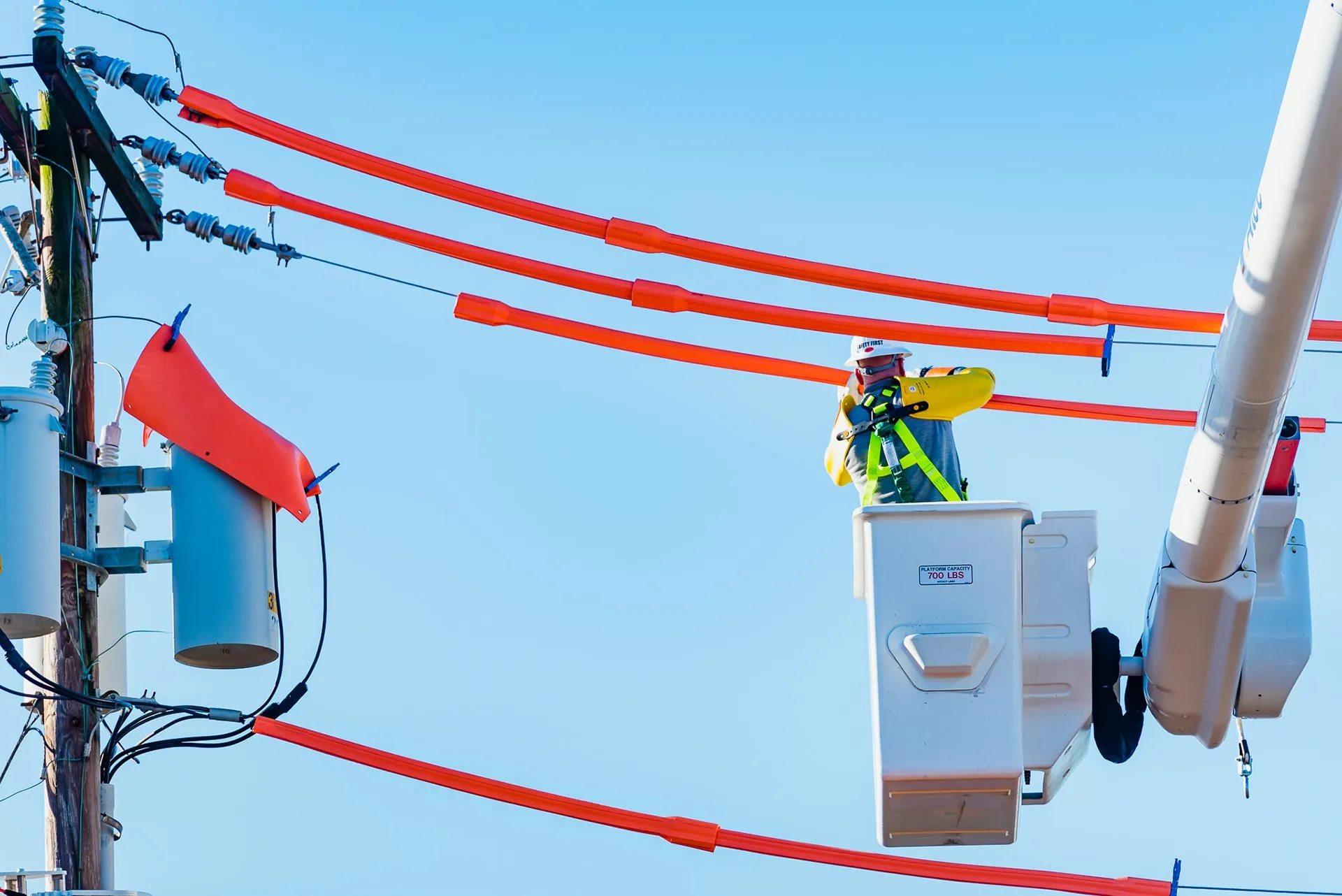 Lineworker in a bucket truck beside overhead distribution lines and transformers
