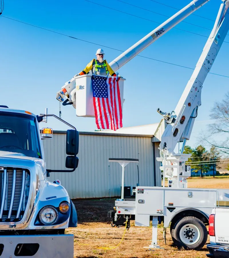 UPA technician in a raised bucket truck holding an American flag