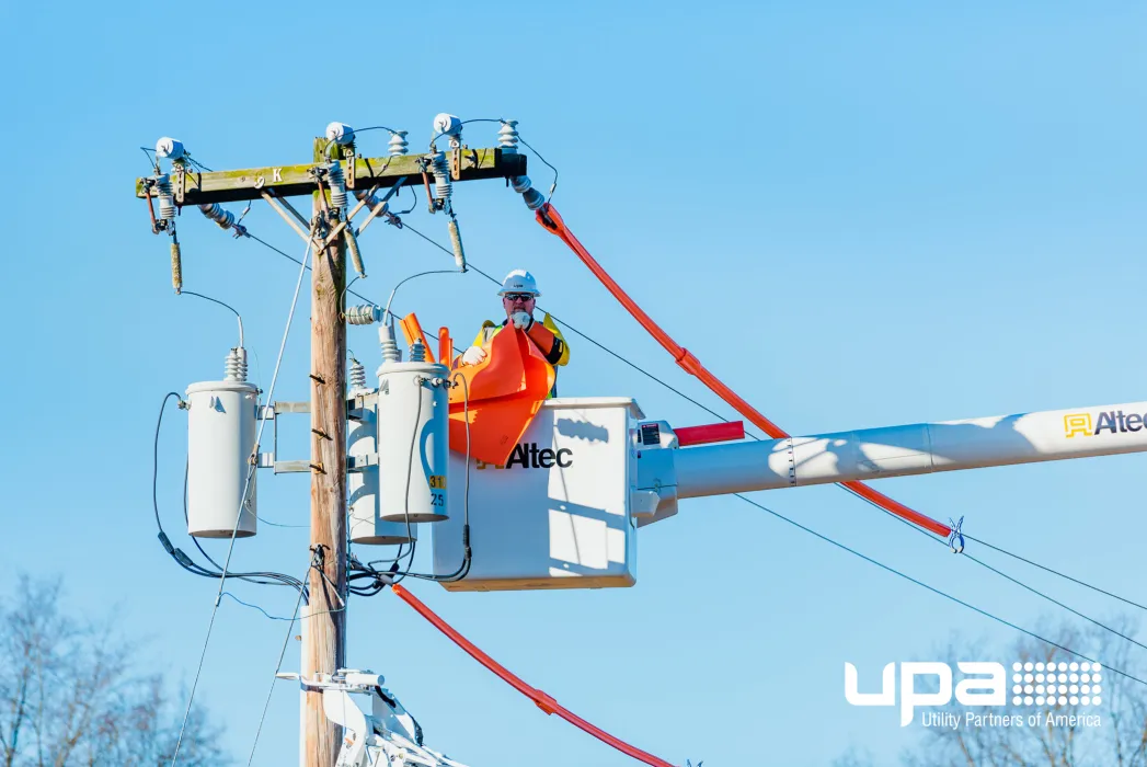 A lineworker in a bucket working at the top of a utility pole with transformers