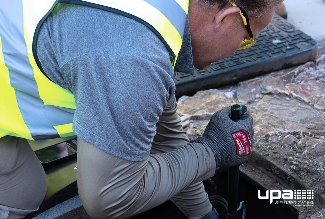 A technician in a high-visibility vest working at an open water meter box